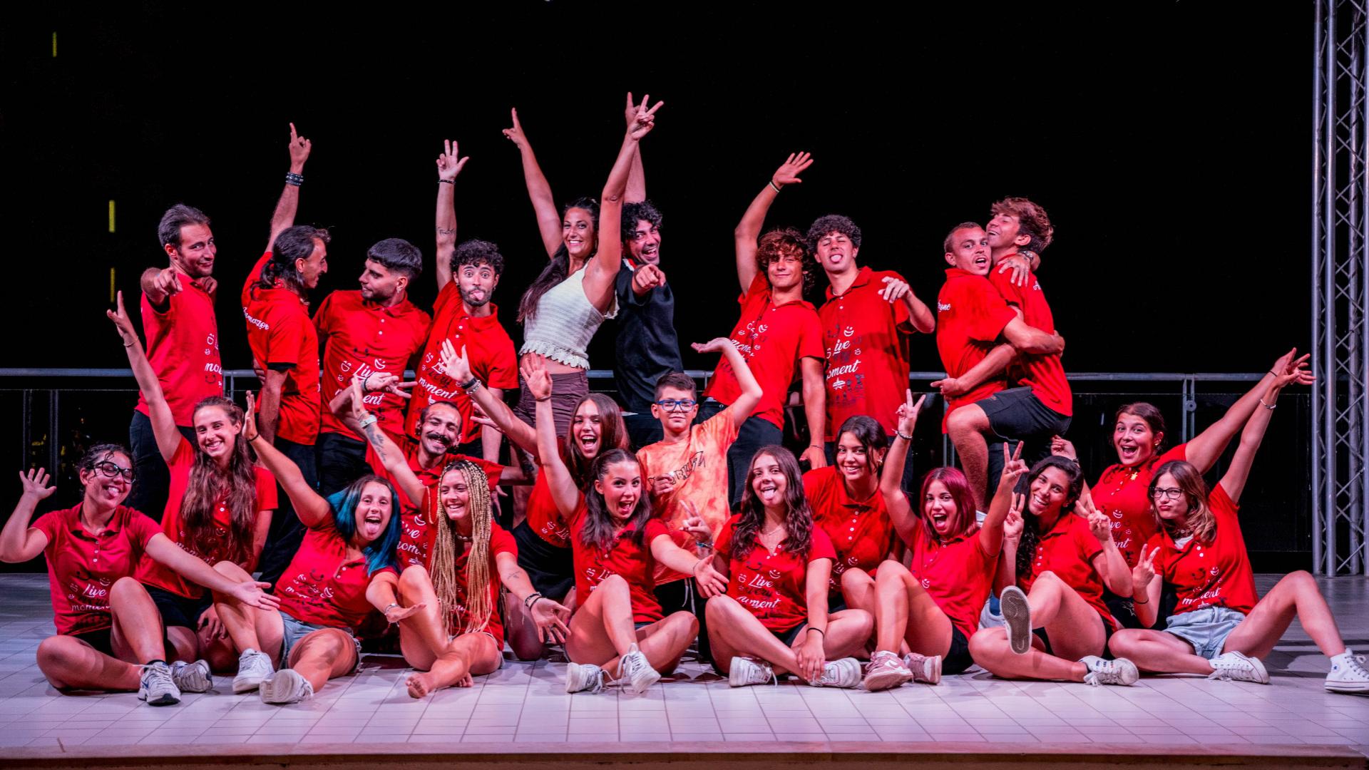 Gruppo di persone in magliette rosse posa allegramente su un palco.