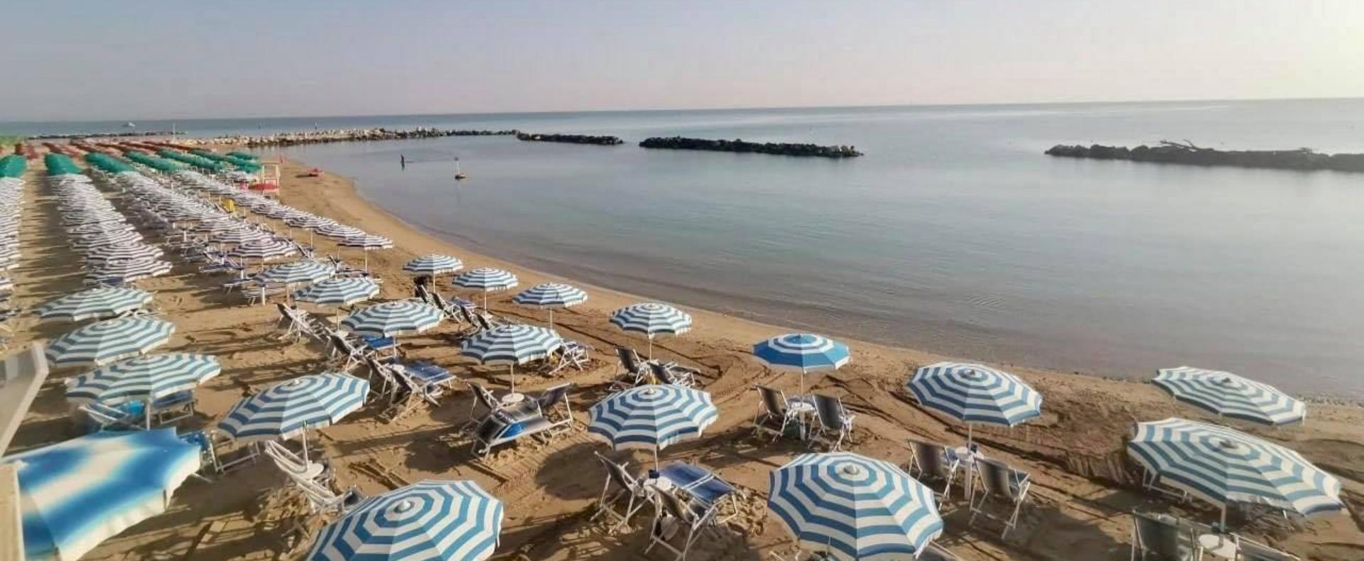 Spiaggia con ombrelloni a righe blu e bianche, mare calmo e cielo sereno.