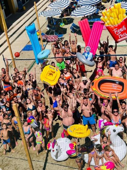 Festa in piscina con persone e gonfiabili colorati, sotto il sole estivo.