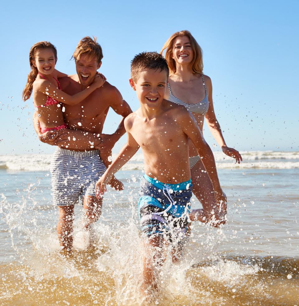 Famiglia felice gioca in acqua sulla spiaggia sotto il sole estivo.