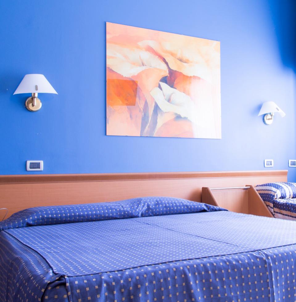 Camera blu con letto matrimoniale e singolo, arte astratta e luci a parete.